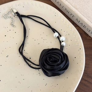 Nahaufnahme des schwarzen Satinrosen-Chokers mit weißen Perlen auf einem Dekoteller