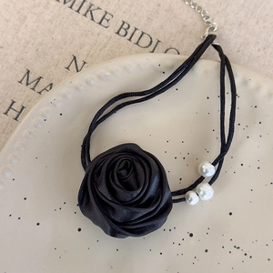Detail eines schwarzen Seidenrosen-Chokers mit weißen Perlen auf einer Keramikplatte