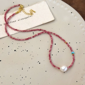 Close-up of beaded necklace featuring pink faceted stones and a baroque pearl detail