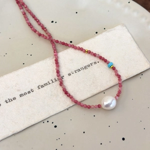 Macro detail of red stone beaded necklace featuring a large baroque pearl and turquoise bead