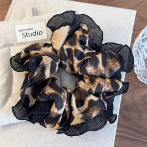 Detail of leopard print hair scrunchie with black lace trim on a minimalist aesthetic background