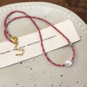 Detail of red faceted stone necklace with baroque pearl and golden lobster clasp closure