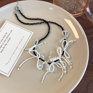 Elegant black and white beaded bow necklace with tassels on a ceramic display tray