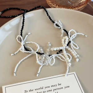 Detailed view of a black and white beaded necklace with crystal bows on a ceramic tray