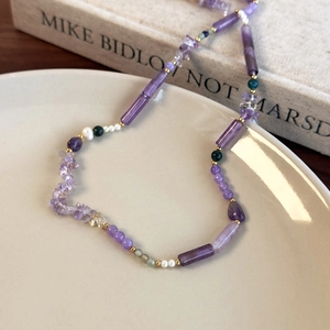 Close-up of a beaded necklace featuring purple stones and pearls on a ceramic dish