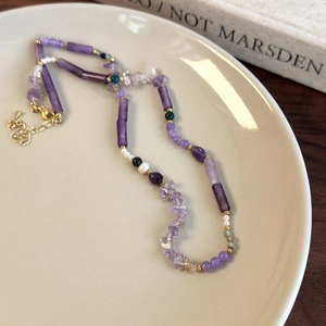 Detail view of purple stone beaded necklace with pearls and gold beads on a ceramic plate
