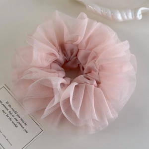 Detailed close-up of a pink tiered lace scrunchie on a minimalist cream background