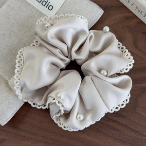 Detailed close-up of cream satin scrunchie with lace trim and pearls on wood