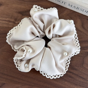 Detail of elegant cream satin scrunchie with lace trim and pearls on a wooden desk