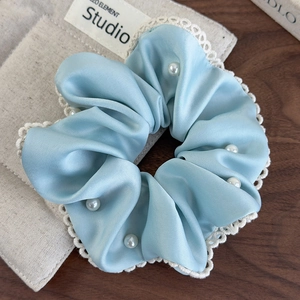 Detail of light blue satin scrunchie with delicate lace edges and pearl embellishments