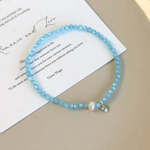 Détail d'un bracelet en perles bleu clair avec une perle blanche et un pendentif en cristal