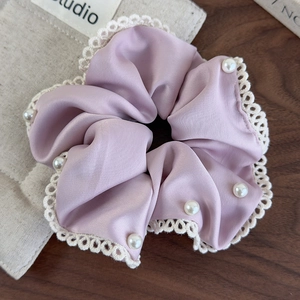 Close-up of lavender satin scrunchie with lace edges and pearl details on wood surface