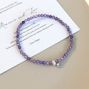 Détail du bracelet en perles de cristal violet avec perle blanche et pendentif clair