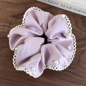 Close-up of lilac satin scrunchie with cream lace trim and pearl accents on wood