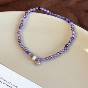 Détail du bracelet en cristal violet avec perle blanche et pendentif sur plateau céramique