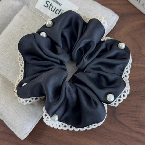 Detail of a black satin scrunchie with white lace edges and pearl accents on fabric
