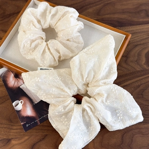 Close-up of beige floral embroidery on gauzy scrunchies and large bow hair accessories
