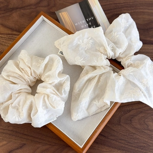 Elegant cream fabric scrunchies with floral embroidery and long ribbons on a display tray