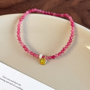 Détail du bracelet en perles de cristal rose avec une perle et un pendentif jaune