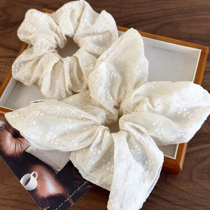Detailed macro view of two white lace floral embroidery organza scrunchies in a tray