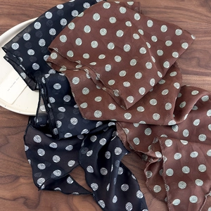 Detail of sheer brown polka dot scarf with fine rolled edges on a wooden surface