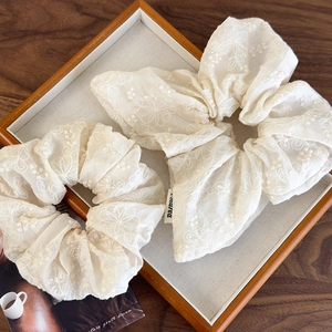 Close-up of beige fabric scrunchies with delicate floral embroidery on wooden tray