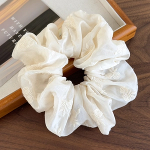 Close-up of beige fabric scrunchie with delicate floral embroidery on wooden texture