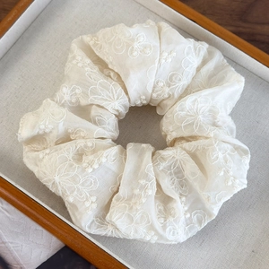 Close-up detail of beige scrunchie featuring elegant white floral embroidery on soft fabric