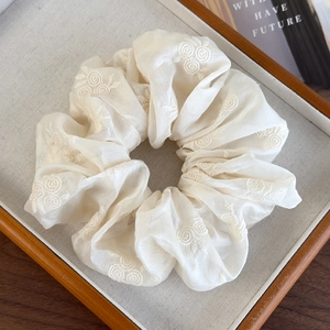 Detailed view of off-white fabric scrunchie with intricate floral embroidery on wooden tray