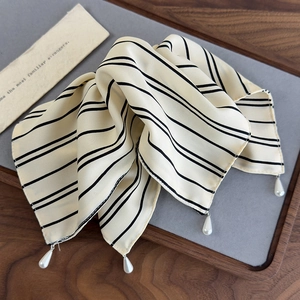 Detail eines cremefarbenen Seidenschals mit Streifen und eleganten Perlenanhängern
