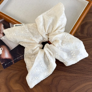 Close-up of beige embroidered floral scrunchie with French style bow on wood tray