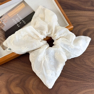 Detail of cream fabric scrunchie with floral embroidery on a wooden tray