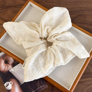 Close-up of beige fabric scrunchie with detailed white floral embroidery in a wooden tray