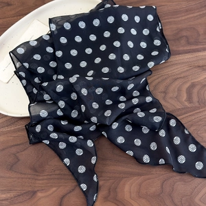 Detailed close-up of a black and white polka dot chiffon silk scarf on a wooden surface