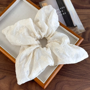 Detail showing off-white fabric scrunchie with delicate floral embroidery on wood tray