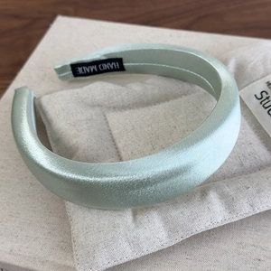 Detail of mint green satin sponge headband with a handmade label on a soft fabric background