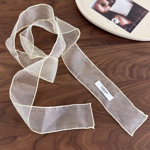 Détail d'un foulard en organza crème avec bordure délicate et étiquette mode sur bois