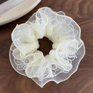 Nahaufnahme von beigem Organza-Haargummi mit Blumenstickerei auf dunklem Holztisch
