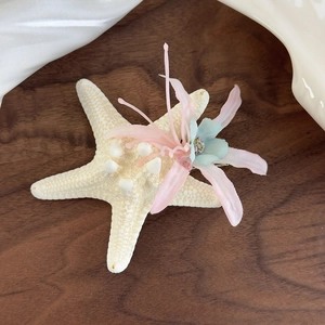 Detailed view of ocean-style starfish hair clip with silk flowers on a wooden tray