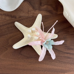 Detail of starfish hair clip with fabric flowers and beads on a rustic wooden background