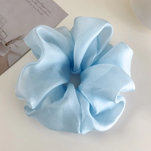 Macro shot of oversized baby blue satin scrunchie showing glossy texture and pleats