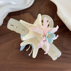 Detail of starfish hair claw with preserved flowers and pink rhinestone on wood surface