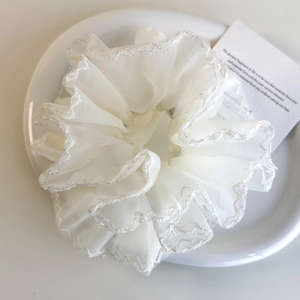 Détail d'un chouchou en organza blanc avec bordure argentée ondulée sur une assiette