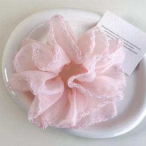 Détail d'un chouchou en organza rose clair avec des bords ondulés sur une assiette en céramique