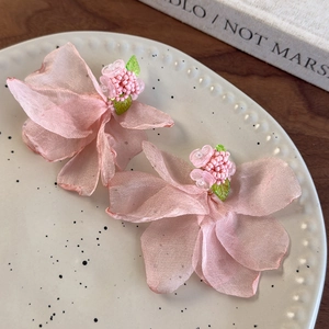 Détail de boucles d'oreilles pétales en mousseline rose avec perles sur un plateau