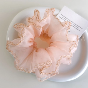 Détail d'un chouchou en organza rose clair avec des bords brodés ondulés champagne sur plat