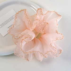 Détail d'un chouchou en organza rose avec bordures dorées sur plateau blanc