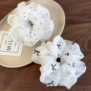 Gros plan de chouchous en organza blanc à pois et motifs nœuds sur un plateau céramique