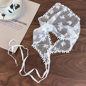 Detail of white lace scarf featuring floral embroidery and wavy edges on dark wood