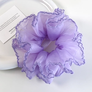 Détail macro du chouchou en organza lavande avec bords festonnés et texture plissée élégante